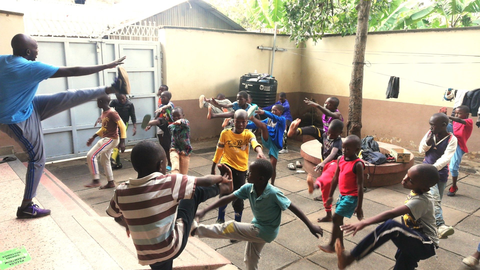 Ein Betreuer und Kinder machen im Hof gemeinsam Kicks und Bewegungsübungen