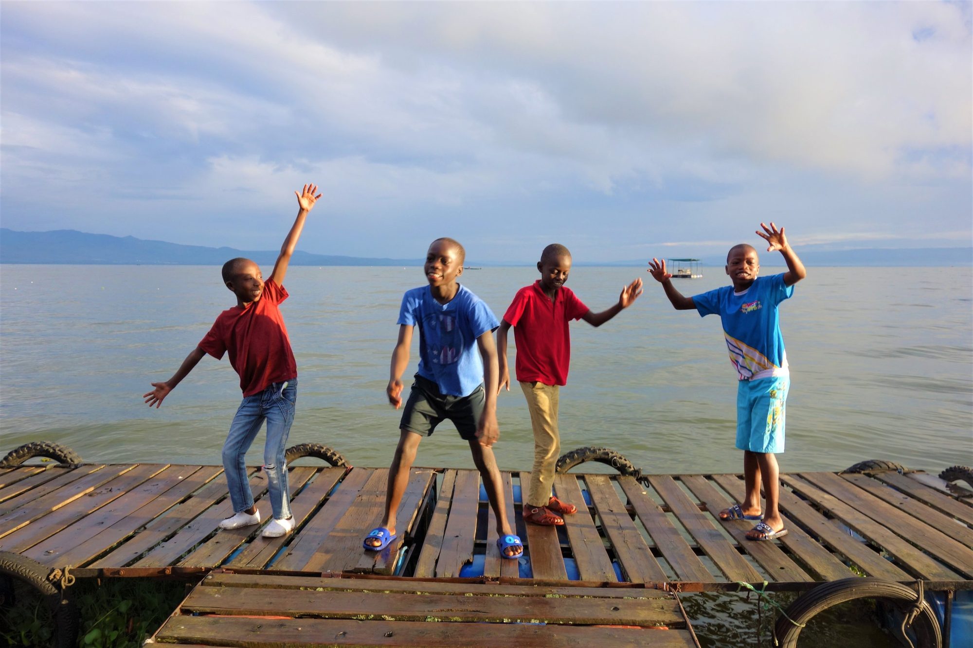 Vier Jungen tanzen und winken auf einem Holzsteg am Lake Naivasha