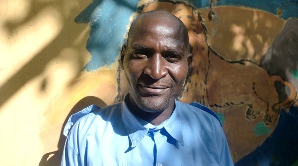 Porträt von Opiyo, Teammitglied im Projekt, vor einem bunt bemalten Wandbild